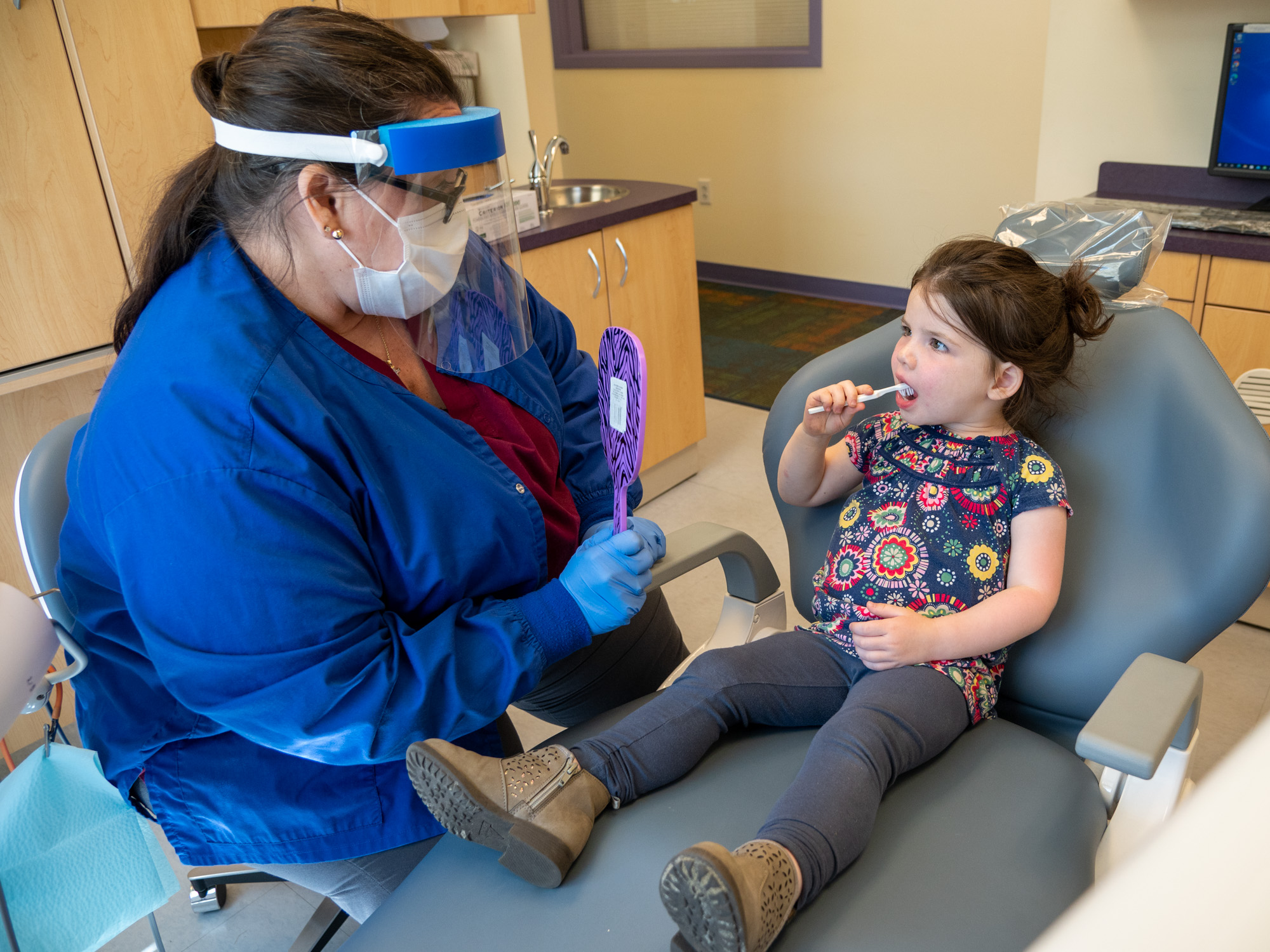 Dental hygenist instructs a child how to brush their teeth.