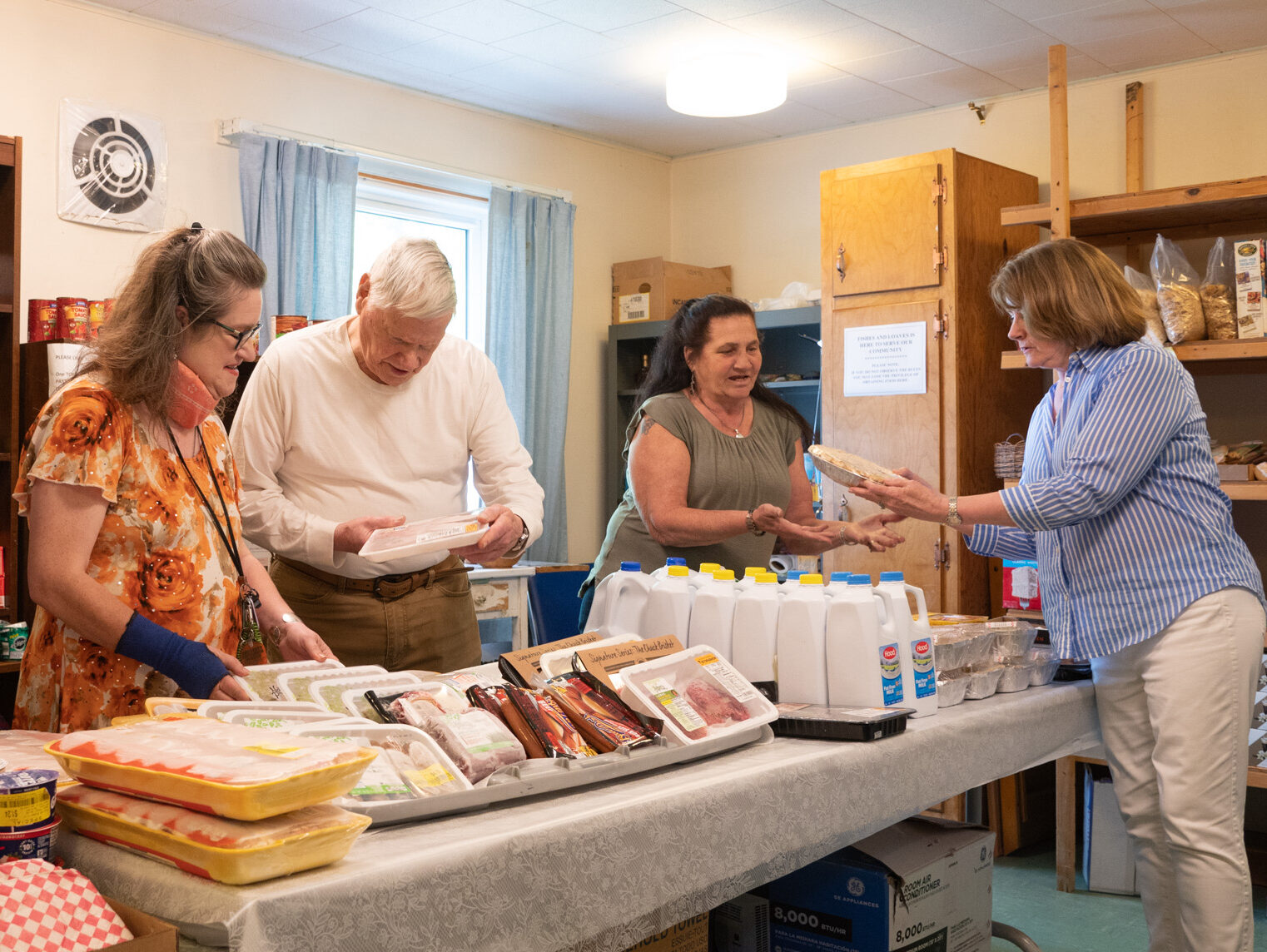 Volunteers in a food pantry organize meat and dairy items on a table.