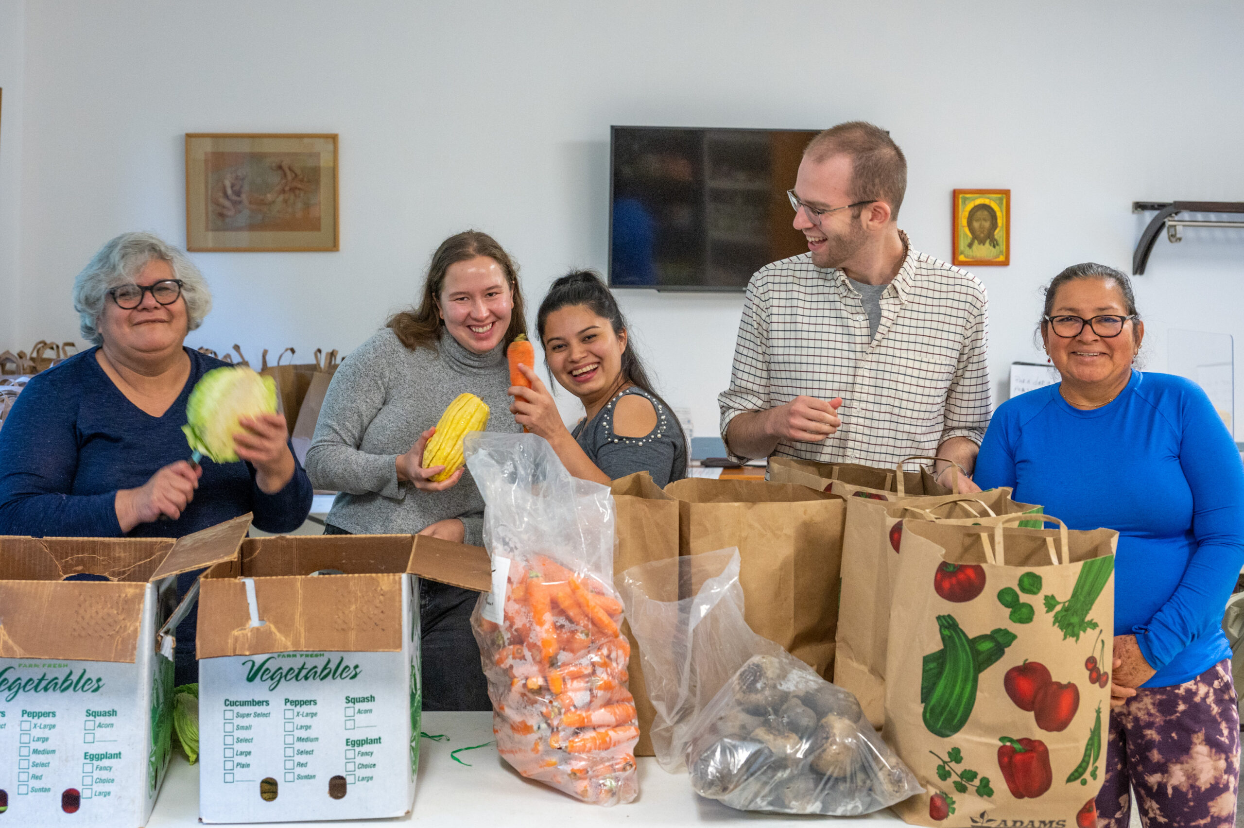 Staff at North East Dutchess Immigrant Services smiles while standing at a table being used to sort fresh produce.